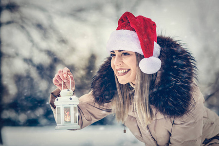 年轻快乐的女人在圣诞老人帽子拿着圣诞灯笼户外在美丽的冬天雪天圣诞节时间