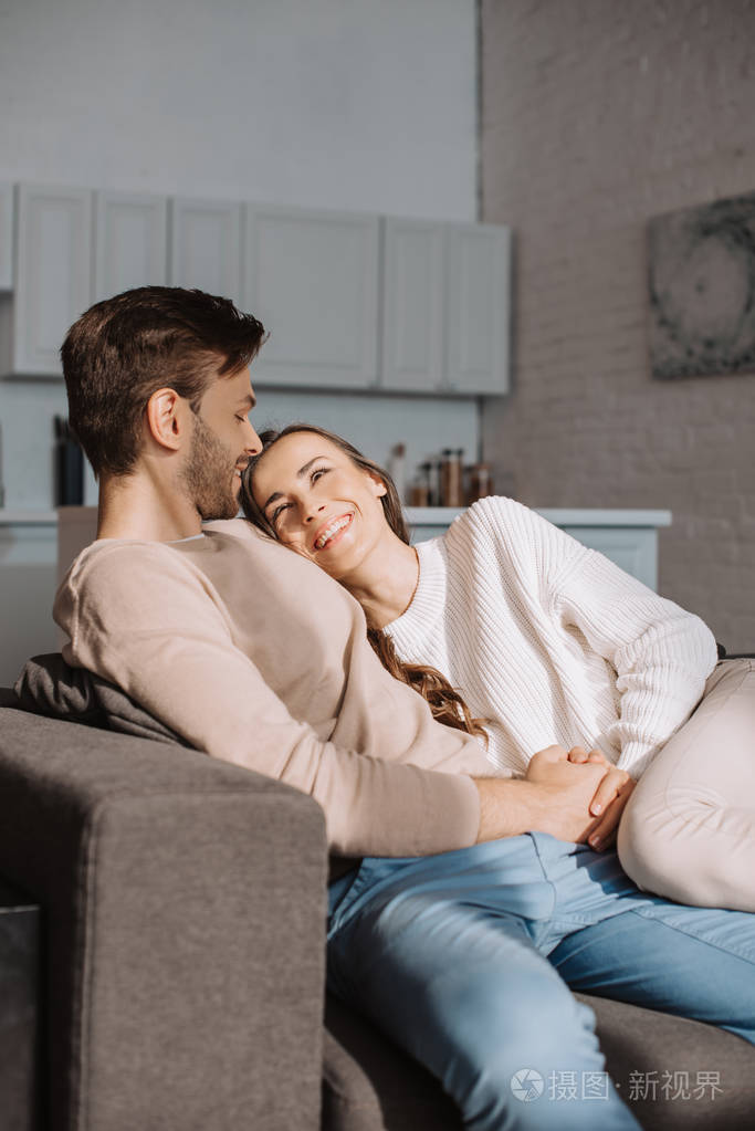 微笑浪漫的年轻夫妇在家里的沙发上调情