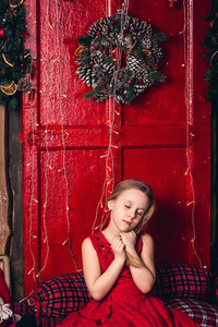 穿着红裙子的女孩坐在门边, 带着圣诞花环