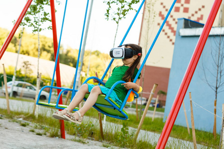 带着虚拟现实耳机的孩子坐在操场秋千上
