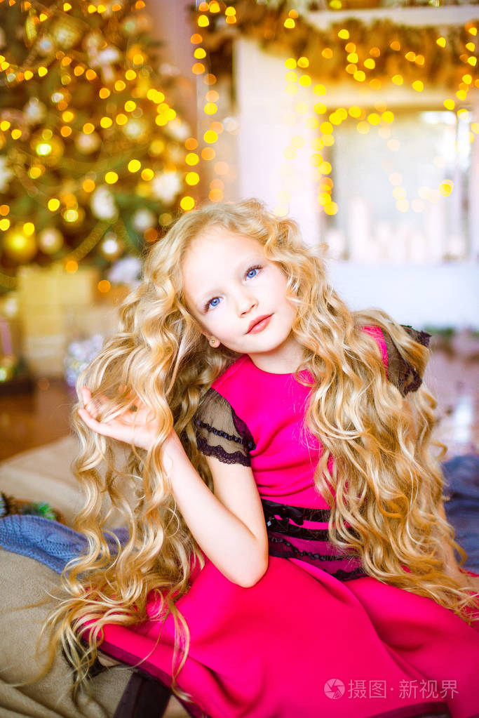 可爱的小女孩与长卷发金发在家里附近的圣诞树与礼品和花环和装饰的