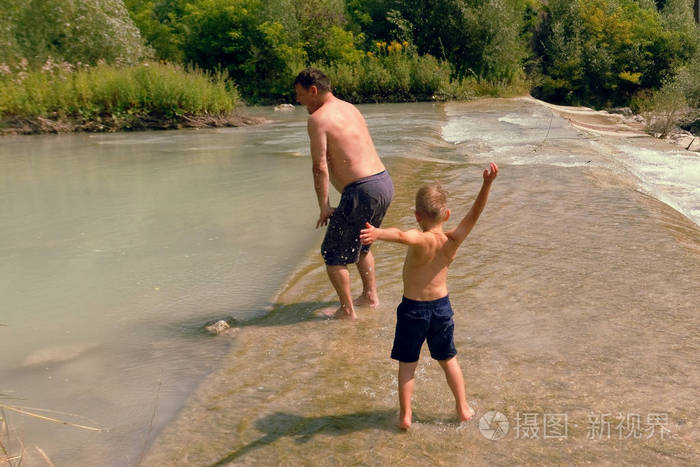 爸爸和儿子在夏天在晴朗的日子里在山河里洗澡
