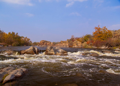 石头在一条快速的河流在秋天的黄色树木在岸边