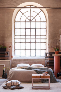 枕头旁边的木桌在床的前面与毯子在 wabi sabi 卧室内部与窗口。真实照片