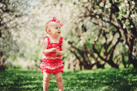 可爱的开心宝贝女孩有趣的粉色爬衣行走户外在春天的花园。快乐的童年概念