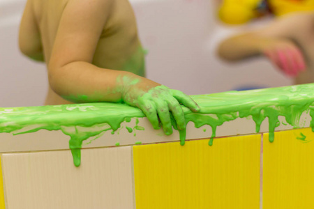 孩子在浴室里玩耍, 用手指画, 浴室在油漆里, 绿色的油漆从墙上流下来. 婴儿的手在绿色的油漆里