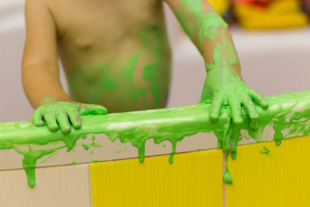 孩子在浴室里玩耍, 用手指画, 浴室在油漆里, 绿色的油漆从墙上流下来. 婴儿的手在绿色的油漆里