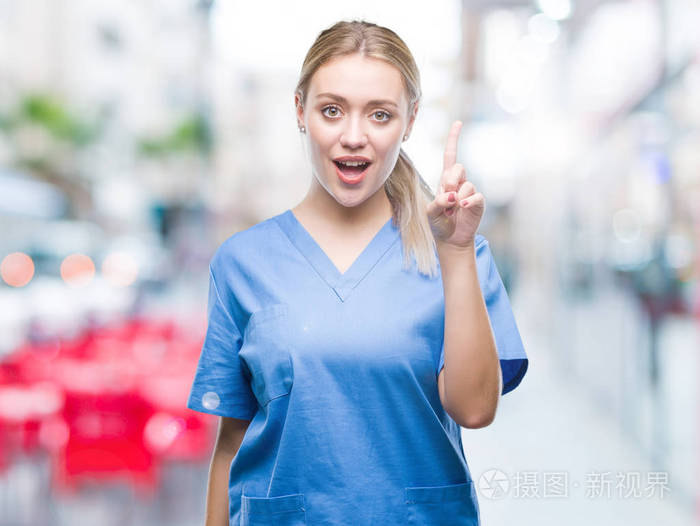 年轻的金发医生医生妇女穿医疗制服在孤立的背景指向手指与成功的想法。退出和快乐。第一个