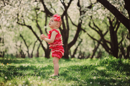 可爱的开心宝贝女孩有趣的粉色爬衣行走户外在春天的花园。快乐的童年概念