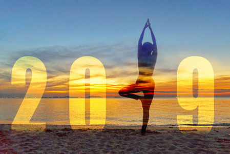 瑜伽新年快乐卡2019。剪影生活方式的妇女练习瑜伽站作为数字2019年的一部分, 在日落时的海滩。健康与度假理念