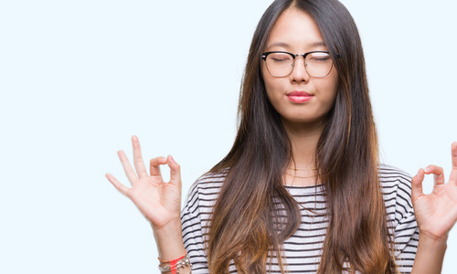 年轻的亚洲妇女戴着眼镜在孤立的背景下放松和微笑闭上眼睛做冥想手势用手指。瑜伽理念