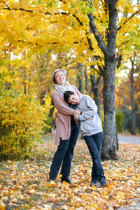 母子在秋城公园。他们是父母摆姿势, 微笑, 玩耍和乐趣。明亮的黄色树