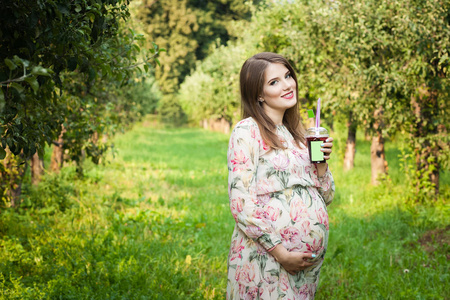 怀孕的女人独自行走在一片草地和喝果汁