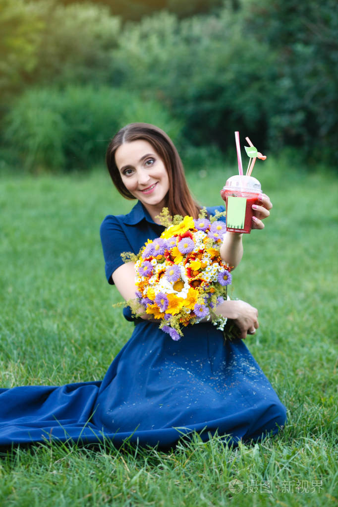 一件蓝衣服的女人是坐在草地上用鲜花和喝果汁