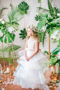 可爱的小女孩, 金发碧眼的卷发在白色的婚纱礼服和花圈的花朵装饰品, 由热带树叶, 白玫瑰和兰花
