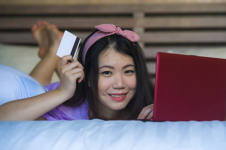 年轻美丽快乐的亚洲女性在笔记本电脑上使用信用卡网上银行在家里微笑着愉快的购物网上购买电子商务和生活方式的概念