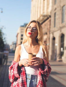 年轻女子拿着一杯咖啡站在街上