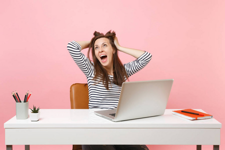 年轻的欣喜若狂的女人执着于头发, 头完成工作完成项目与 pc 笔记本电脑, 而坐在办公室查出的柔和粉红色背景。成就事业的事业理念