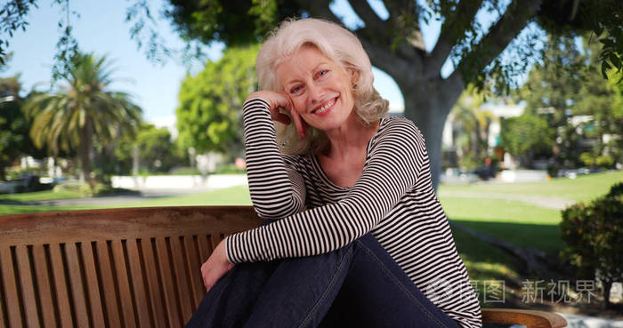 在公园的好日子里她脸上摆着快乐表情的老太婆在长椅上摆姿势