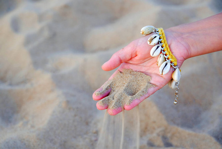 一个温柔的女孩的手的特写镜头, 手镯是由贝壳制成的。在水的背景下。背景模糊。通过手指的沙子