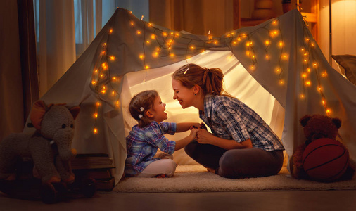 幸福的母亲和女儿在帐篷里在家玩耍