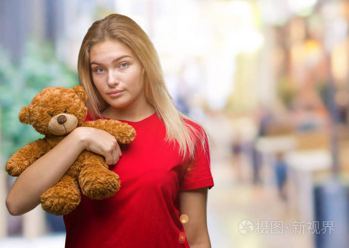 年轻的白种女人抱着可爱的泰迪熊在孤立的背景与自信的表情在聪明的脸思考严重