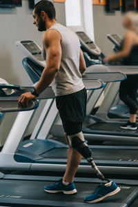 英俊的年轻运动员与人工腿行走在踏板上在健身房