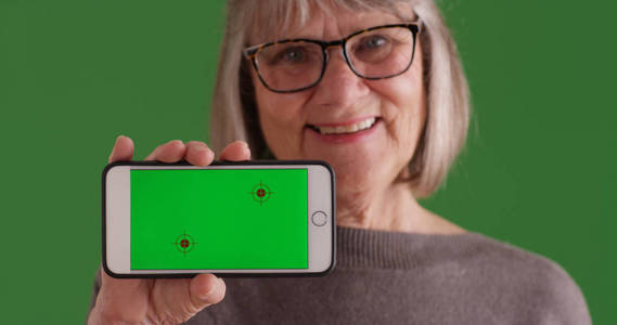 由老年妇女在绿色屏幕上举行的带绿色屏幕显示屏的智能手机