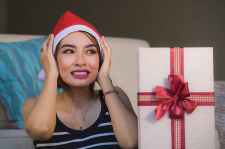 年轻美丽和快乐的女人在圣诞老人帽子拿着红色丝带微笑愉快和兴奋地在家里客厅接受或准备圣诞礼物在假日生活方式