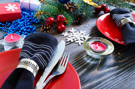 圣诞餐桌设置。红色盘子, 叉子, 刀, 蜡烛, 餐巾纸, 礼物树枝上的圣诞树上的一个黑暗的木制的背景。圣诞节和新年假期背景