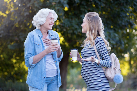 快乐怀孕的妇女享受与年迈的母亲在户外的谈话