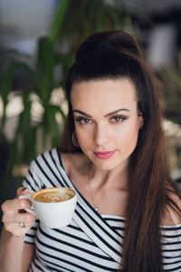 一个女人在一家咖啡馆，捧着一杯咖啡或卡布奇诺的特写肖像
