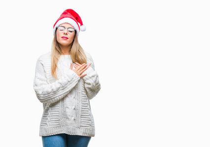 年轻美丽的妇女戴着圣诞节帽子在孤立的背景微笑与手在胸部与闭的眼睛和感恩的手势在脸上。健康理念