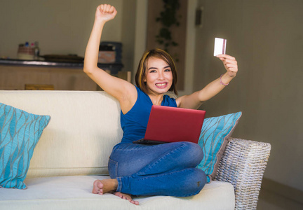 年轻美丽和快乐的女人在家客厅拿着信用卡使用笔记本电脑银行和网上购物微笑轻松在电子商务和互联网商业概念
