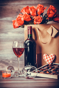 红酒瓶, 一盒巧克力, 两杯葡萄酒, 玫瑰在一个纸袋里, 用红色的心装饰在木桌上。情人节庆祝概念。复制空间