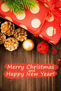 圣诞节和元旦节日装饰, 金球, 金杉木锥, 树枝与礼物包裹在红色的纸与金色圆圈在棕色木头背景。平躺着。从上面看文字圣诞快乐, 新