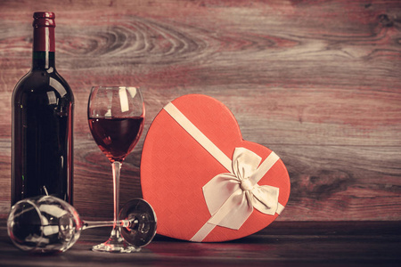 红酒瓶, 两杯葡萄酒和礼物心脏在木桌上。情人节庆祝概念。复制空间