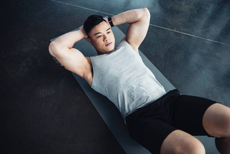 年轻的亚洲运动员在健身房的健身垫上做腹肌运动