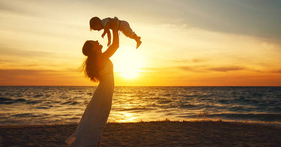 快乐家庭母亲和婴儿的儿子走过海洋总和在海滩上