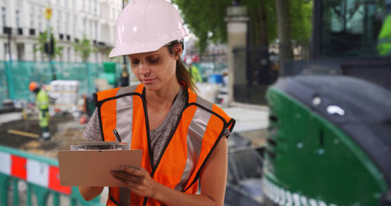 身穿安全背心的女建筑工人在工作地点使用剪贴板