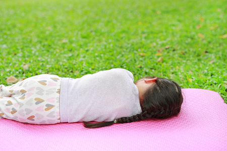 在夏季公园花园, 在绿草如茵草地上睡在粉红色床垫上的亚洲小女孩