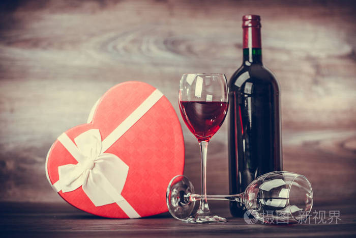 红酒瓶, 两杯葡萄酒和礼物心脏在木桌上。情人节庆祝概念。复制空间