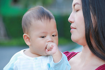 婴儿男婴的肖像正在吸吮手与亚洲母亲携带