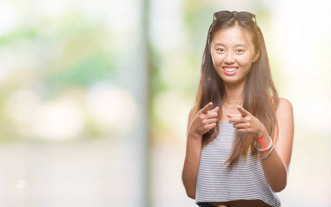 年轻的亚洲妇女戴着太阳镜在孤立的背景下, 手指在相机与快乐和滑稽的脸。良好的能量和共鸣