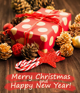 圣诞节和元旦装饰, 球, 冷杉锥, 糖果和星星与礼物包裹在红色的纸与金圆在木头背景与文字快乐圣诞快乐和新年快乐