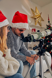 愉快的情侣朋友享受圣诞前夜新年前夜与望远镜在家里