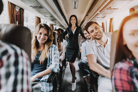 女旅游服务员工在旅游巴士上工作。站在旅游巴士乘客座位上的年轻微笑的女人。旅游旅游和人的概念。旅行中的人。暑假