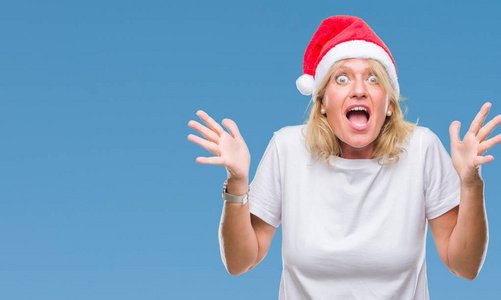 中年金发女子戴着圣诞节帽子在孤立的背景庆祝疯狂和惊讶的成功与双臂举起和睁开的眼睛尖叫兴奋。获奖者概念