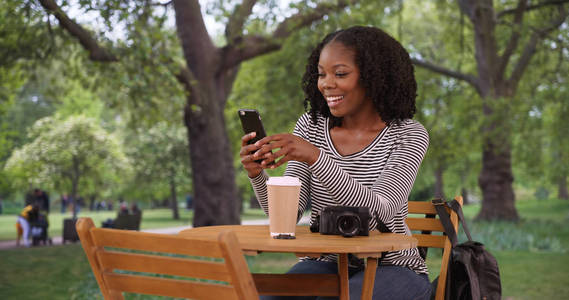 在伦敦圣詹姆斯公园, 可爱的黑人妇女坐在桌旁用智能手机发短信