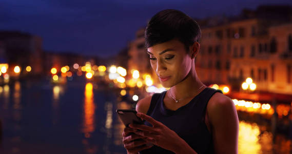 在威尼斯意大利旅行的漂亮的黑人妇女看着她的电话留言面带微笑